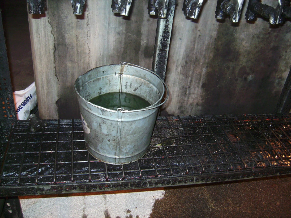 A dirty metal bucket being used to transfer lubricants from storage.